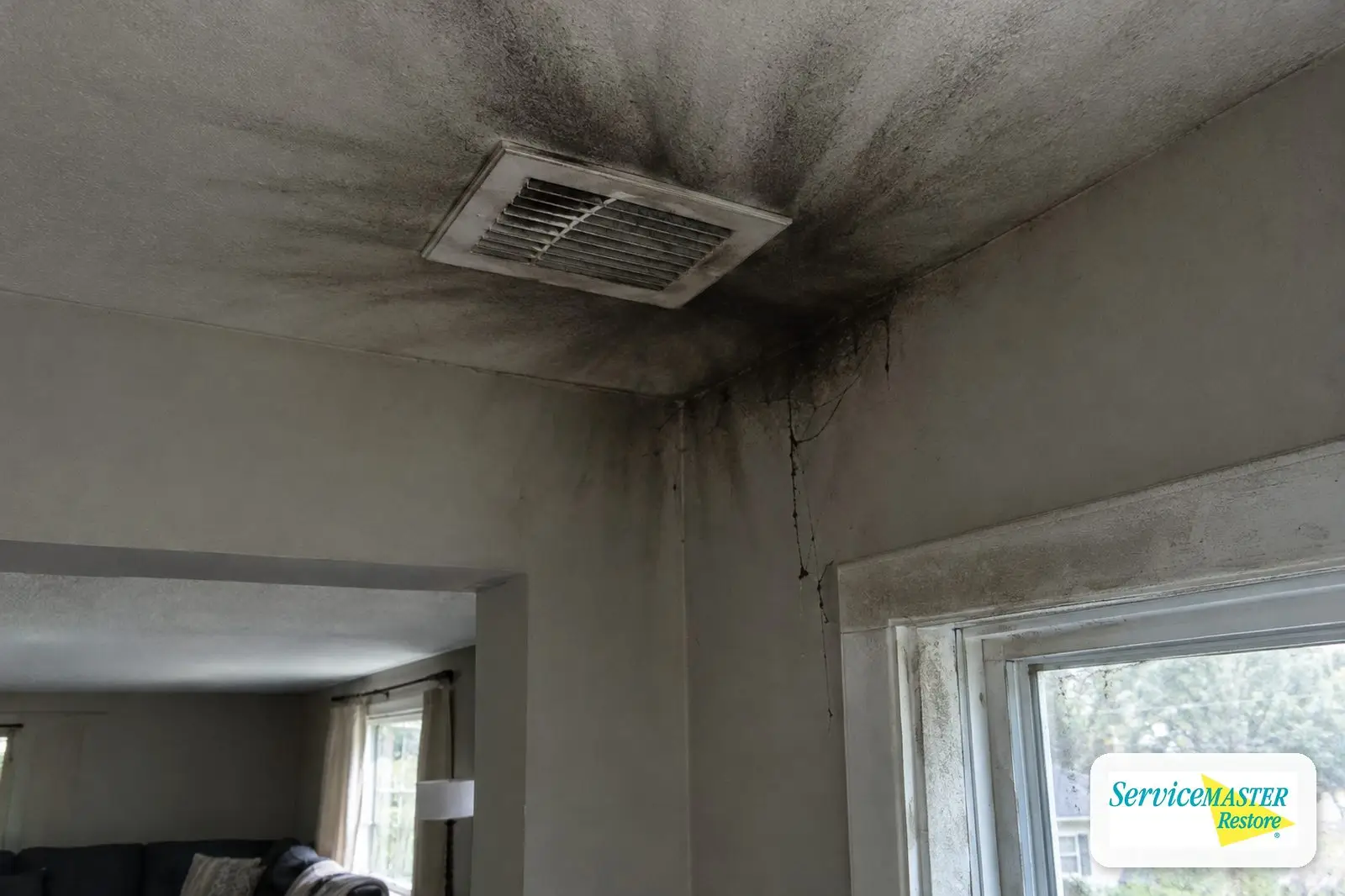 Soot streaks around a ceiling air register and soot webs in a room corner after a furnace puffback