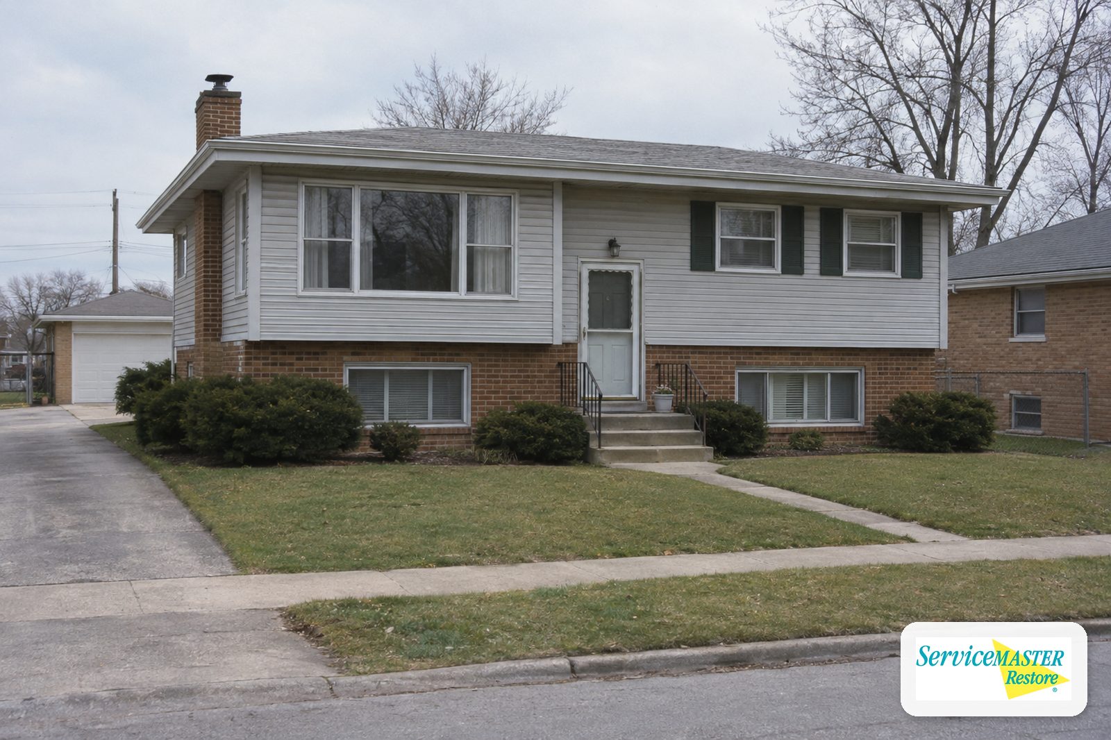 1960s raised ranch home with a brick lower level and siding above on a suburban street